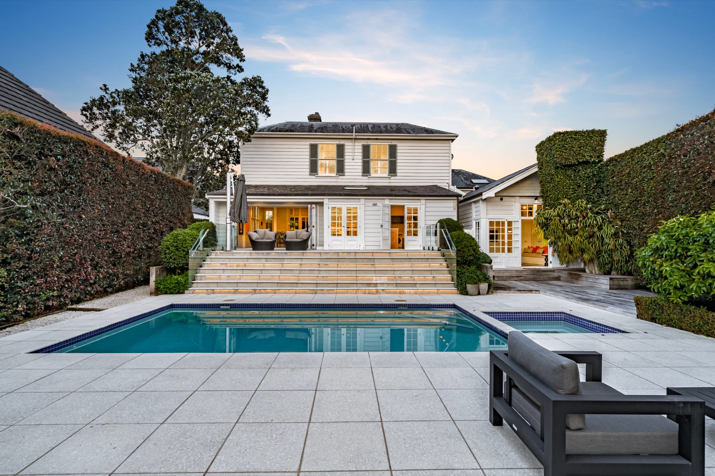 The rear of 52 Bassett Road at dusk, its windows lit above the pool